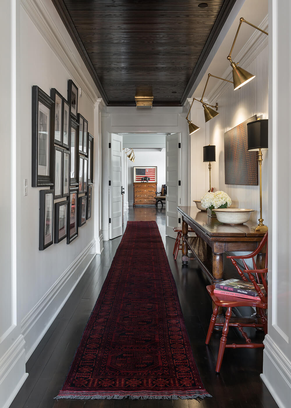 Hallway with framed art, wood console table, and long red patterned runner.