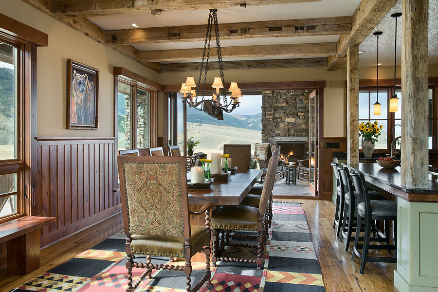Dining room with long wood table and chairs surrounding. A geometric rug underneath. There is wood wainscotting on the walls. The room opens up to the back patio