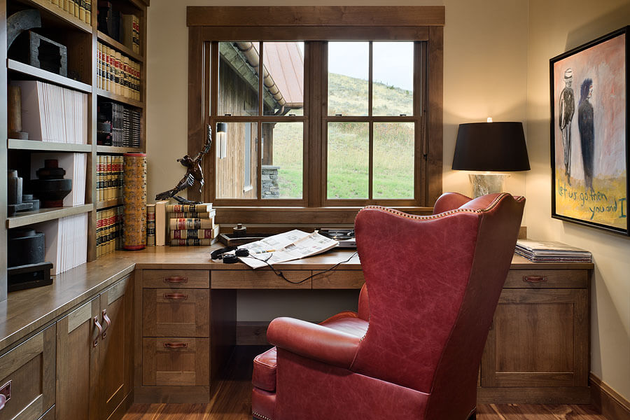 Home office with built-in bookcase and desk, red leather chair, and original artwork